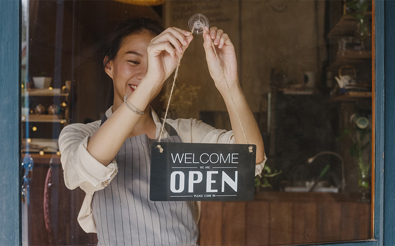 A smiling restaurant owner hanging an open sign on the glass door.